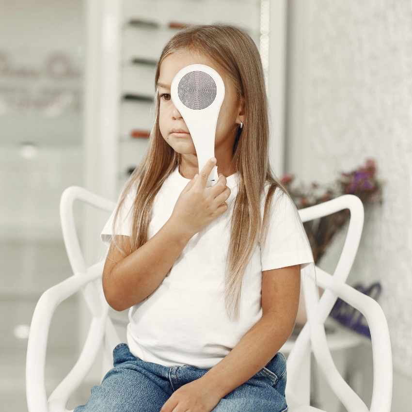 Child holding a white vision therapy occluder with a printed concentric circle pattern over one eye.