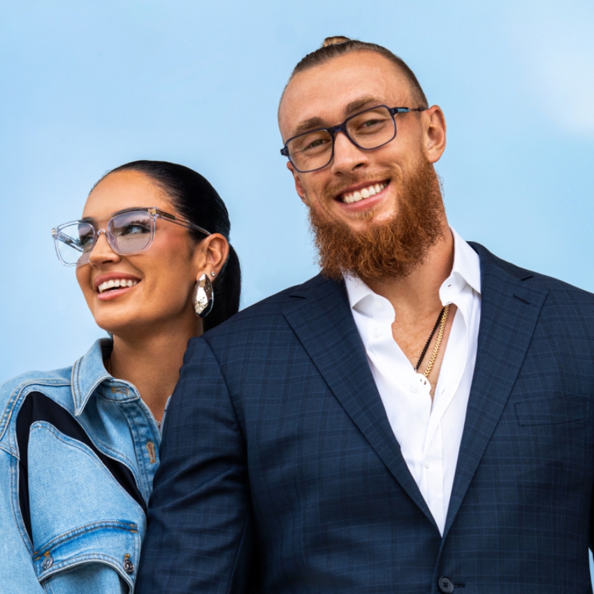 Two people wearing stylish eyeglasses; one in a denim jacket, the other in a dark suit.