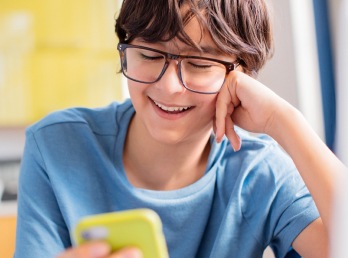 Image of a teenager wearing Zenni glasses, smiling while holding a cell phone.