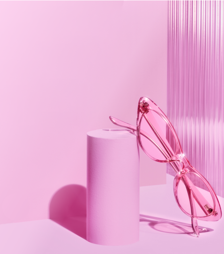 Image of three pair of Zenni glasses displaying on pink block with pink background. From left to right: pink cat-eye, rimless heart-shape glasses with pink lens tints, and pink slim cat-eye frame.