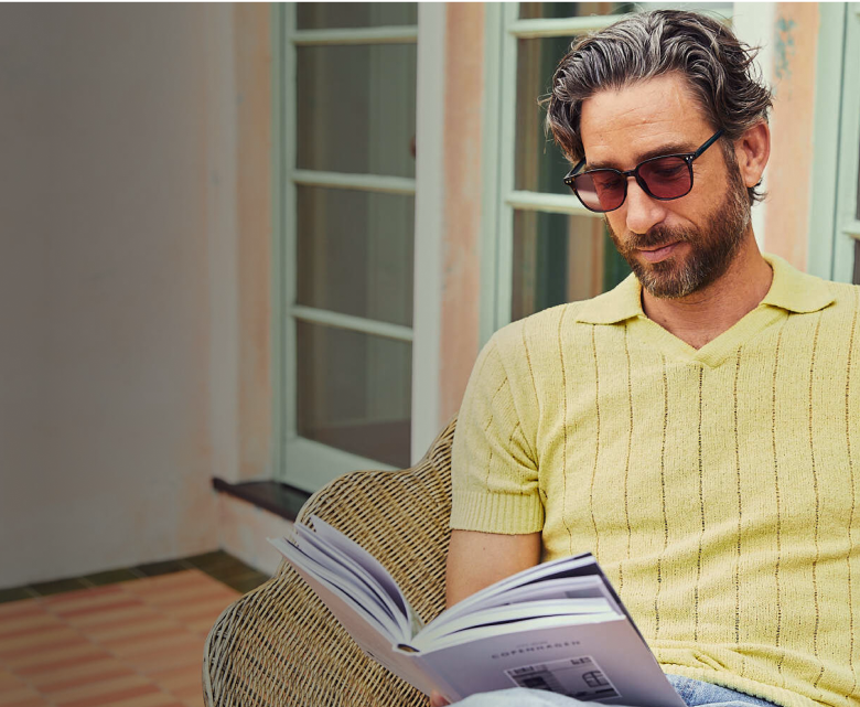 Millennial man wearing glasses for Light Sensitivity and Migraine Relief, reading outdoor