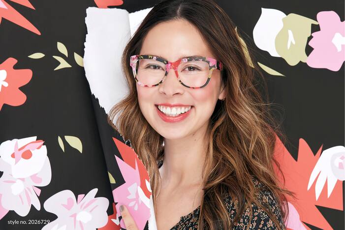 Image of a woman smiling wearing Zenni square glasses #2026729, ripping through patterned paper that matches her glasses.